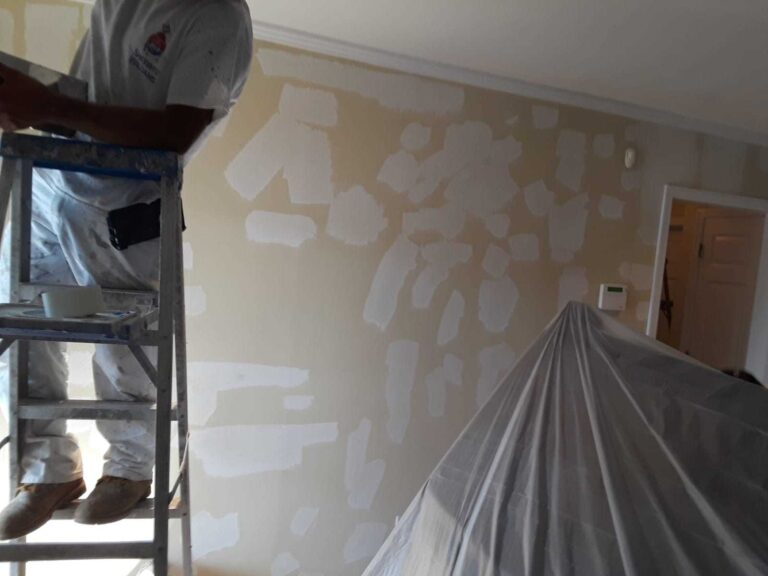 A man applies white paint to the walls of a room, focused on achieving a smooth and even finish.