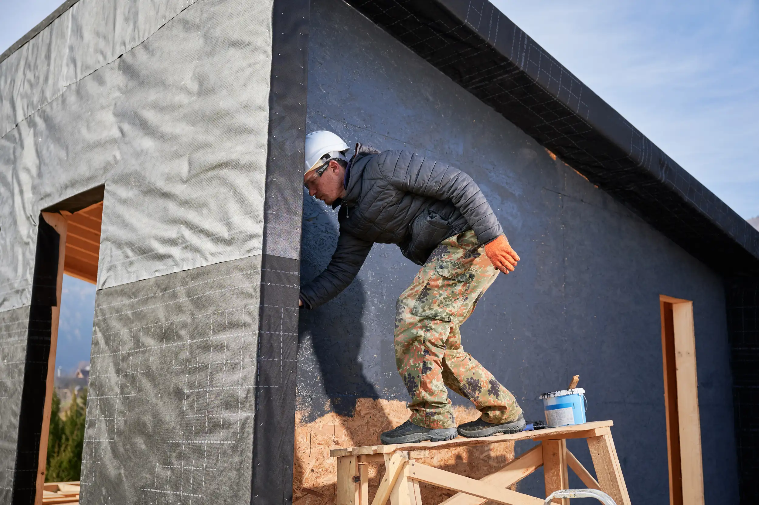 A male worker painting outside of the house with black.