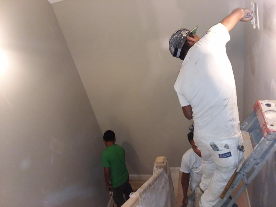 Two men are painting a room in a house, focused on their task with brushes and paint cans in hand.